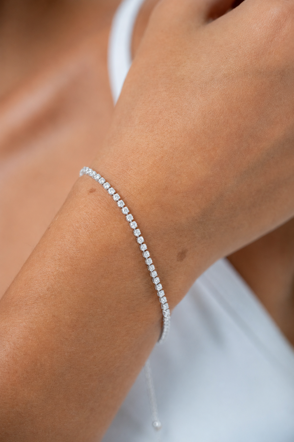 Close-up of a model wearing a delicate gold tennis bracelet with sparkling clear stones.