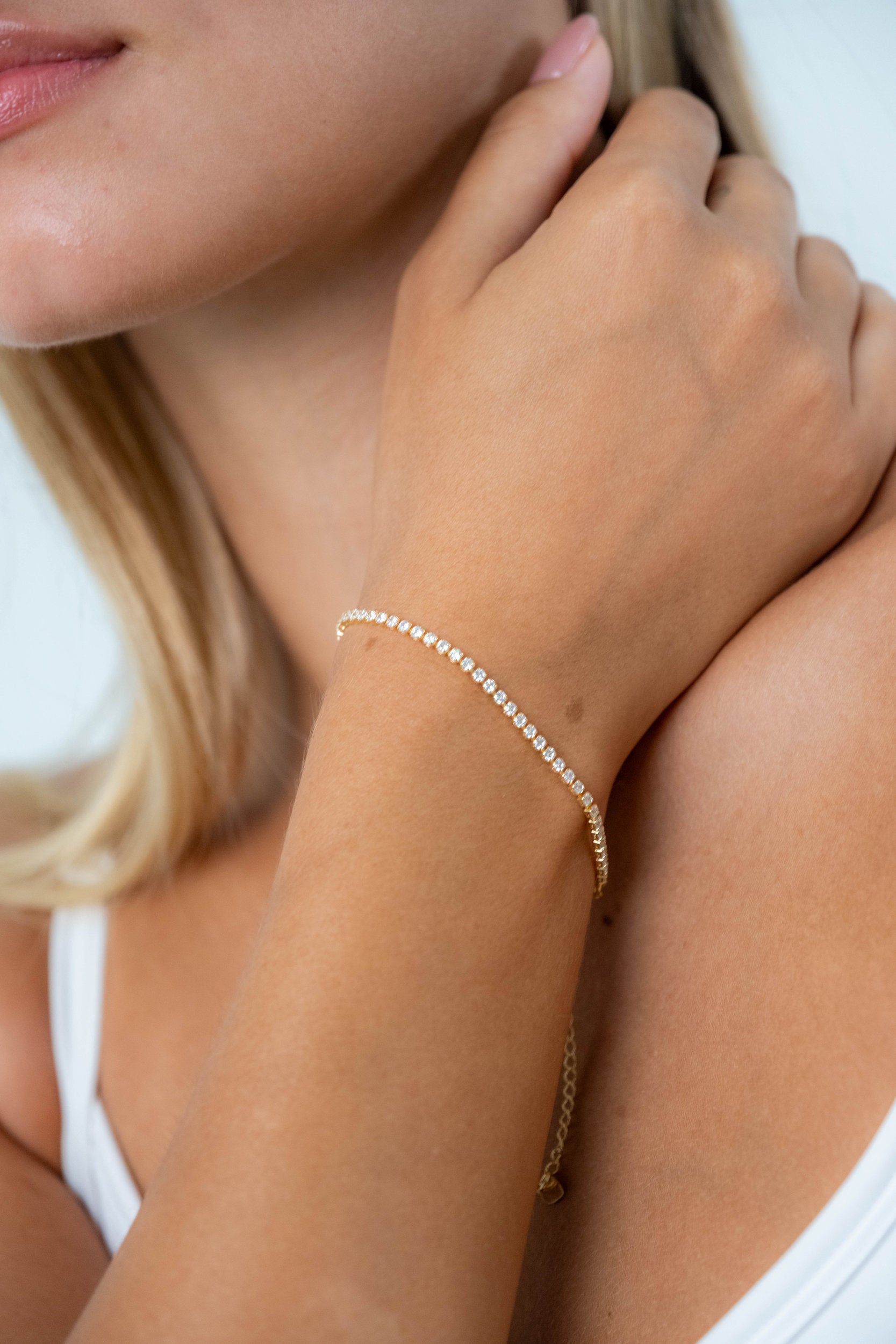Close-up of a model wearing a delicate gold tennis bracelet with sparkling clear stones.