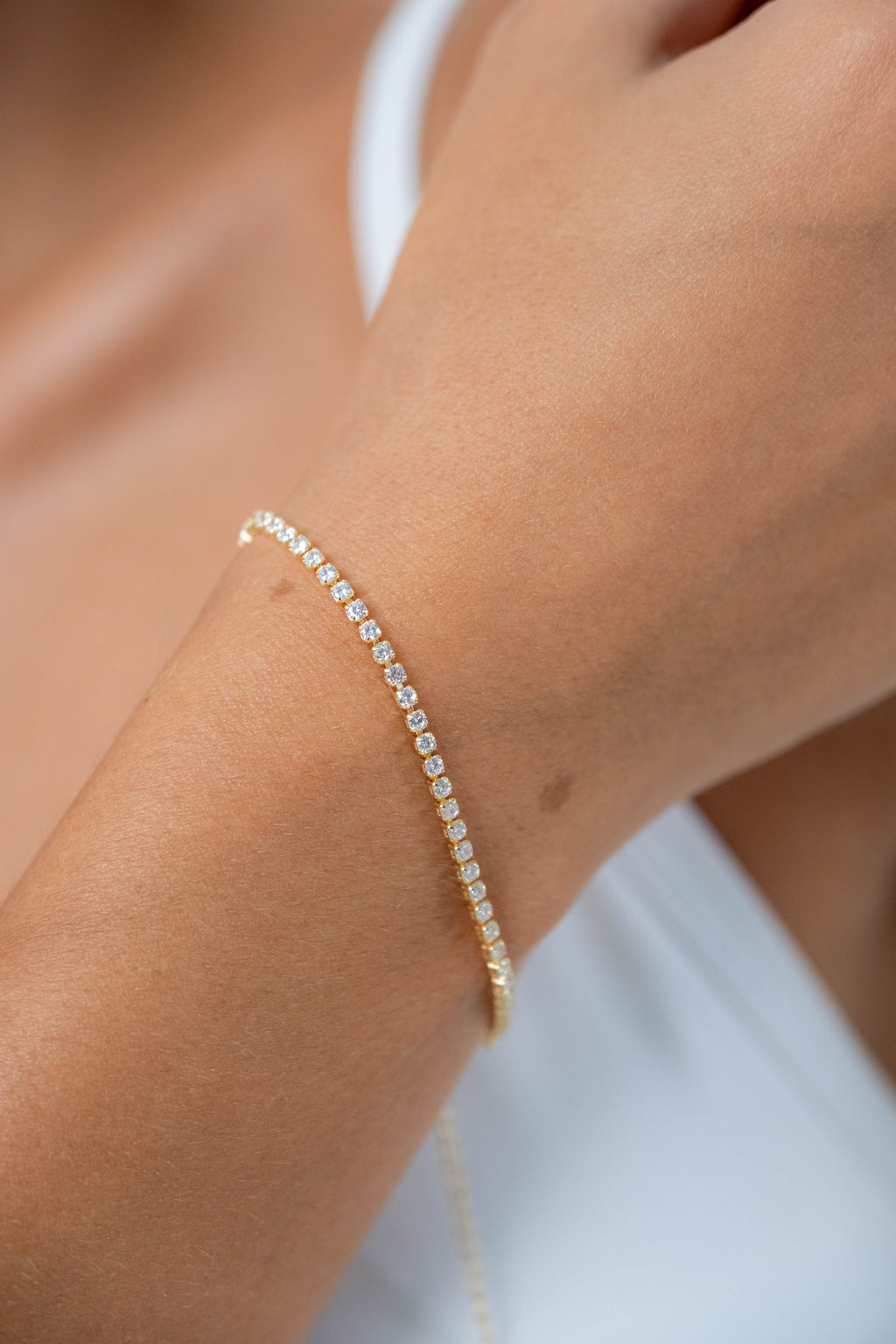 Close-up of a model wearing a delicate gold tennis bracelet with sparkling clear stones.