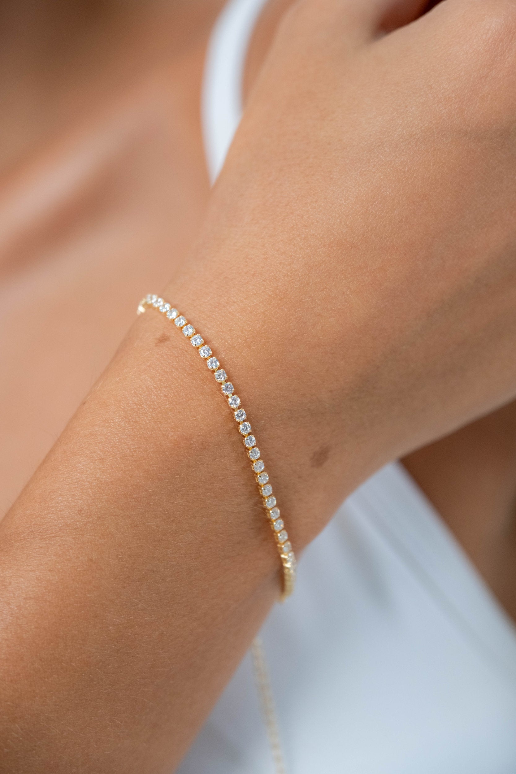 Close-up of a model wearing a delicate gold tennis bracelet with sparkling clear stones.